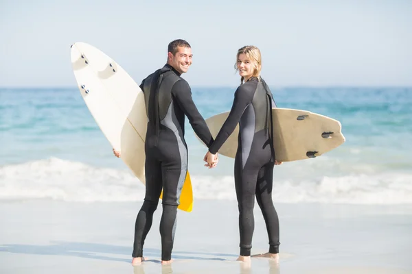 Par med surfbräda håller handen på stranden — Stockfoto