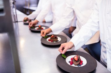 chefs finishing dessert plates in kitchen clipart