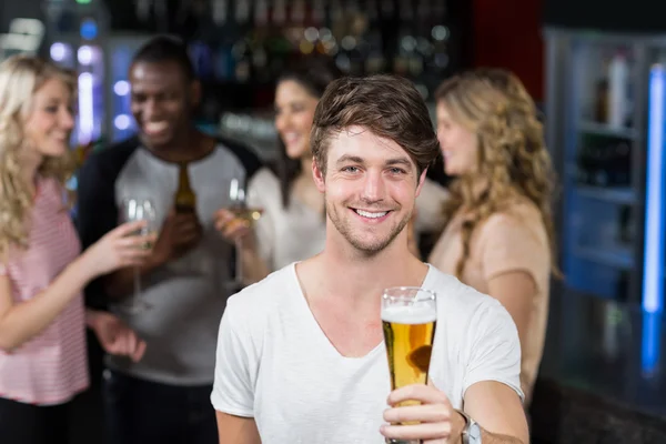 Homme souriant montrant une bière avec ses amis — Photo