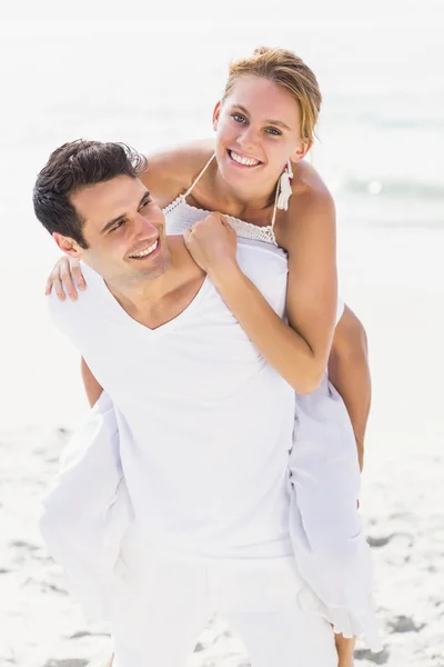 Man giving a piggy back to woman on the beach — Stock Photo, Image