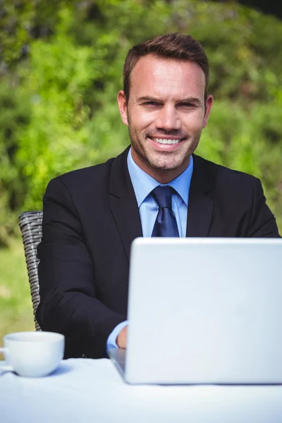 Uomo d'affari sorridente utilizzando il computer portatile e prendendo un caffè — Foto Stock