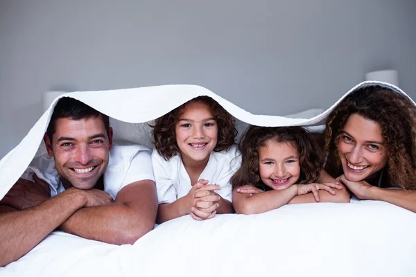 Portrait of happy family lying under a bedsheet — Stock Photo, Image