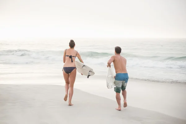 Coppia che corre con una tavola da surf sulla spiaggia — Foto Stock