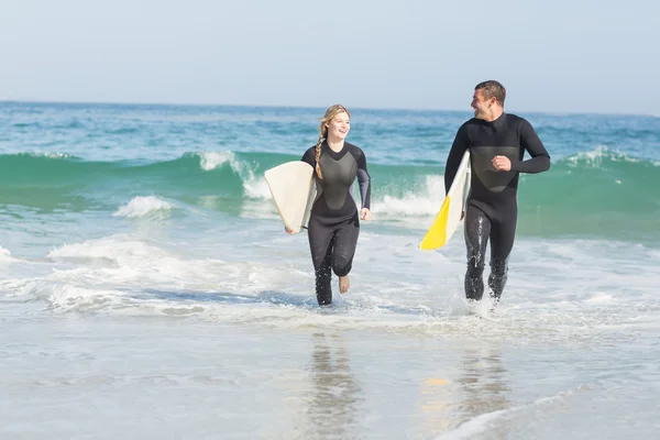 Coppia con tavola da surf corsa in spiaggia — Foto Stock