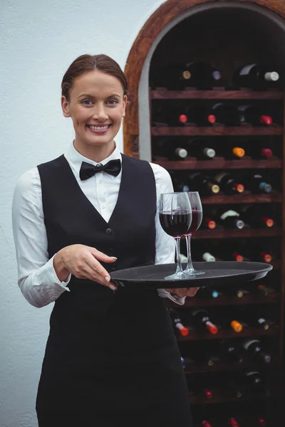 Camarera sonriente sosteniendo una bandeja con copas de vino tinto — Foto de Stock