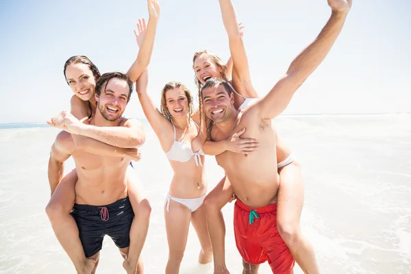 Hombres dando un cerdito de nuevo a las mujeres en la playa —  Fotos de Stock