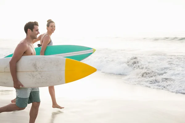 Paar läuft mit Surfbrett am Strand — Stockfoto