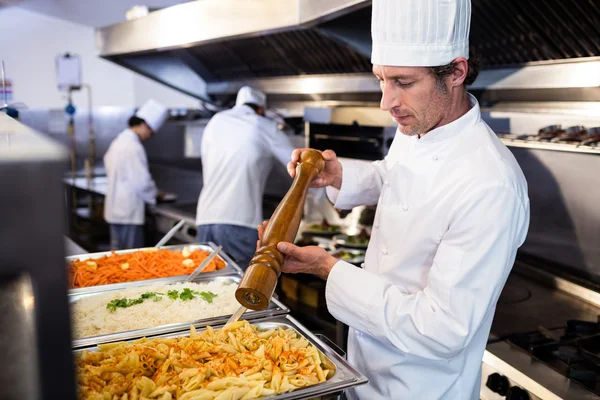 Chef grinding pepper over pasta