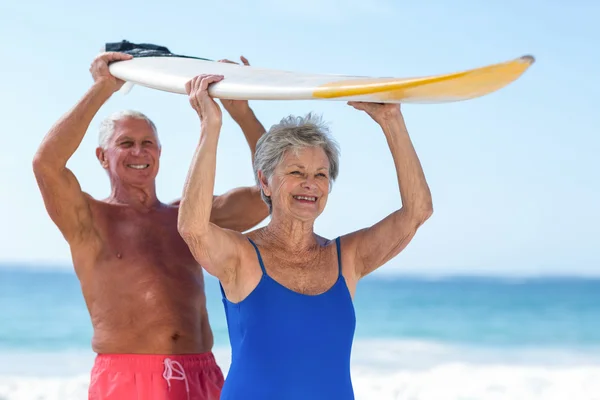 Pareja sosteniendo una tabla de surf sobre sus cabezas —  Fotos de Stock