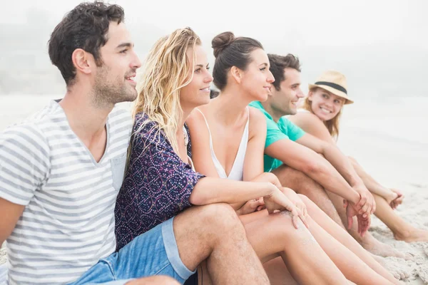 Groupe d'amis assis côte à côte sur la plage — Photo