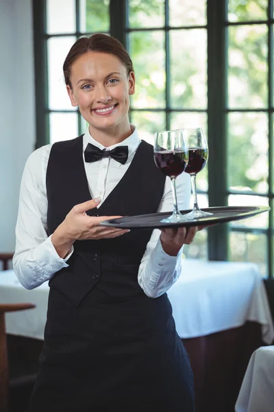 Smiling waitress holding a tray with glasses of red wine — Stock Photo, Image