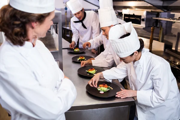 Head chef overlooking other chef decorating dish — Stock Photo, Image