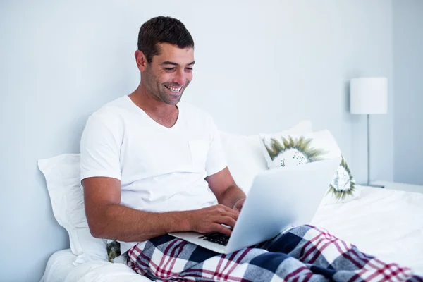 Feliz joven usando el ordenador portátil en la cama — Foto de Stock