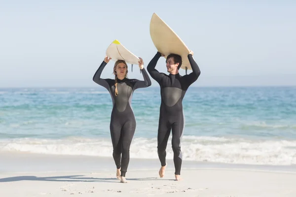 Couple in wetsuit carrying surfboard over the head — Stock Photo, Image