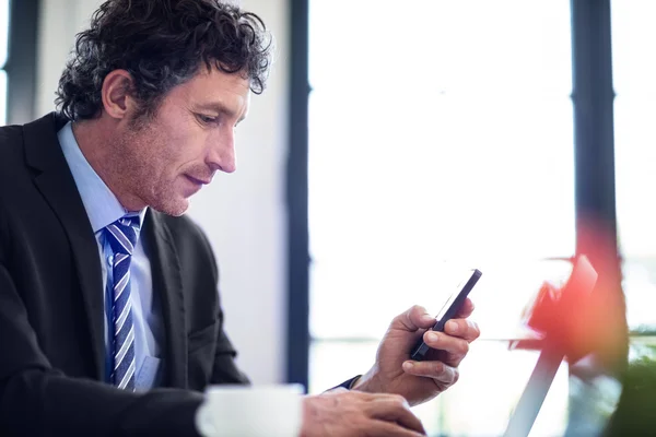 Businessman using phone while working on laptop — Stock Photo, Image