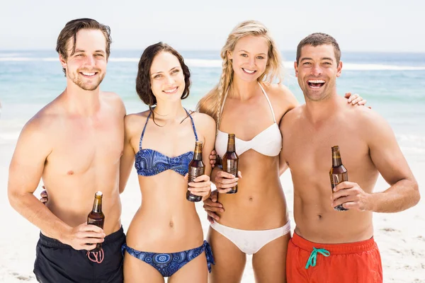 Happy friends standing on the beach with beer bottles — Stock Photo, Image