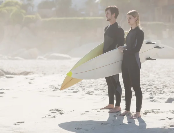 Coppia con tavola da surf in piedi sulla spiaggia — Foto Stock