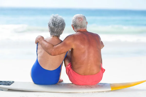 Cute mature couple sitting on a surfboard — Stock Photo, Image