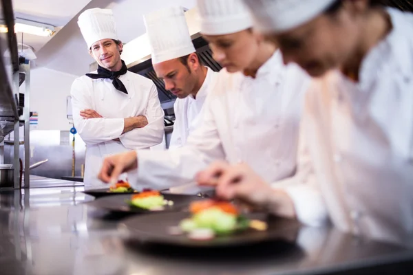 Head chef overlooking other chef preparing dish — Stock Photo, Image