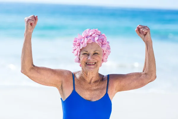 Velmi zralá žena ukazující její svaly na pláži — Stock fotografie