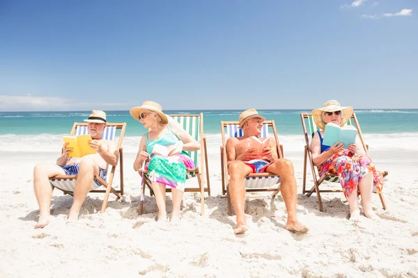 Amigos mayores leyendo libros sobre sillas de playa — Foto de Stock