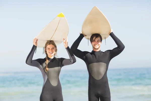 Pareja en traje de neopreno llevando tabla de surf sobre la cabeza —  Fotos de Stock