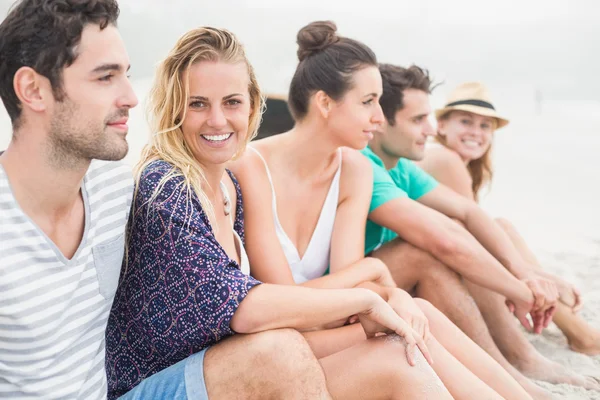 Groupe d'amis assis côte à côte sur la plage — Photo