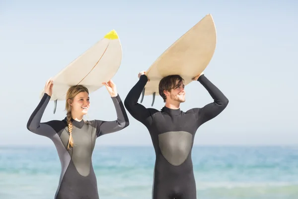 Casal feliz em roupa de mergulho carregando prancha sobre a cabeça — Fotografia de Stock