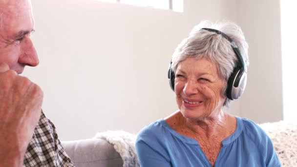 Pareja madura escuchando música con auriculares en el sofá — Vídeos de Stock