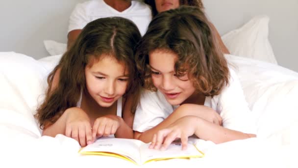 Симпатичные братья и сёстры читают книгу на кровати родителей — стоковое видео