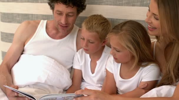 Familie liest ein Buch auf dem Bett — Stockvideo