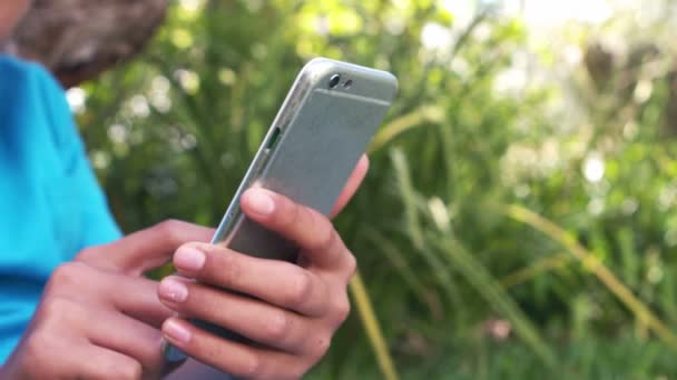 Aranyos fiú használ smartphone ül a fűben — Stock videók