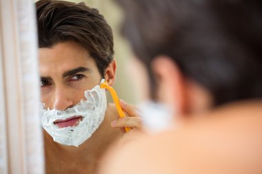 Man reflecting in mirror while shaving beard clipart