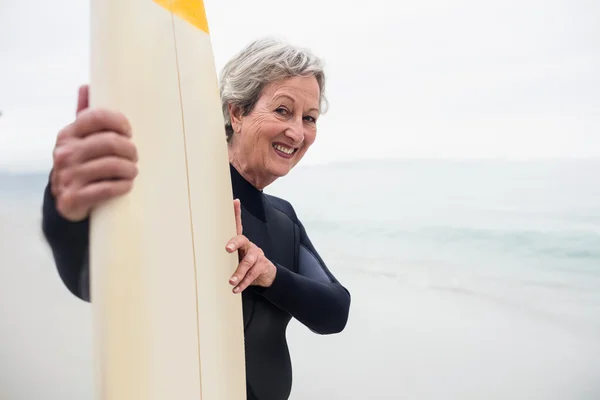 Femme âgée en combinaison tenant une planche de surf — Photo