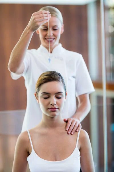 Massagista segurando pingente sobre a cabeça da mulher — Fotografia de Stock