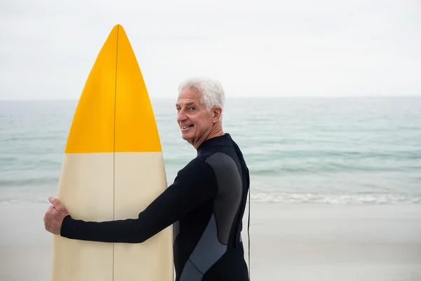 Uomo anziano in muta che tiene tavola da surf — Foto Stock