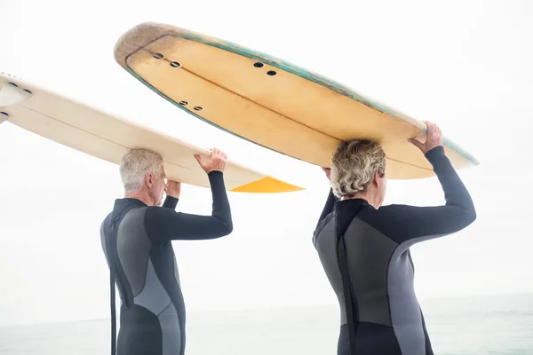 Casal de fato de mergulho carregando pranchas de surf — Fotografia de Stock