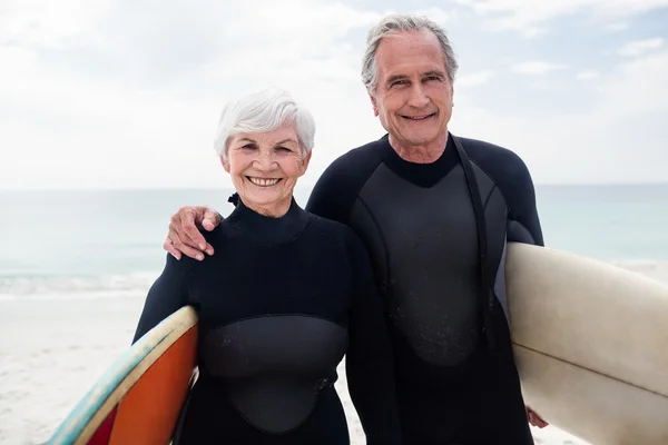 Pareja mayor sosteniendo tabla de surf en la playa —  Fotos de Stock