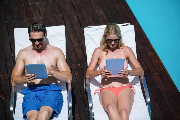 Par med tablett och ligga på solstolar — Stockfoto