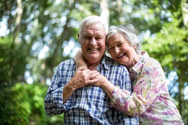 Feliz mujer mayor abrazando desde detrás del marido contra los árboles — Foto de Stock
