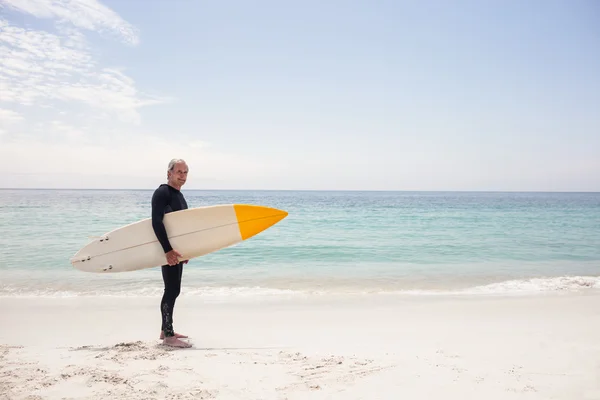 Senior en combinaison tenant une planche de surf — Photo