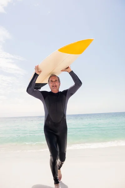 Äldre man i våtdräkt kör med surfbräda — Stockfoto