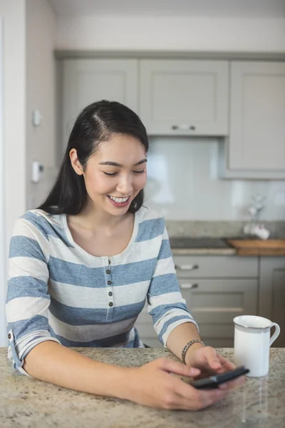 Woman typing on phone in kitchen — Stock Photo, Image