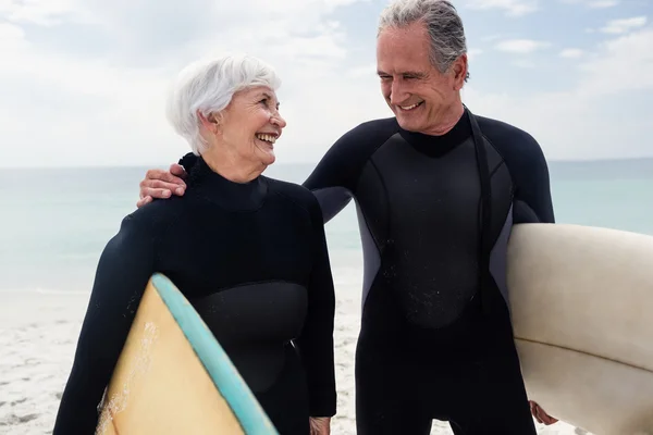 Pareja mayor sosteniendo tabla de surf en la playa —  Fotos de Stock