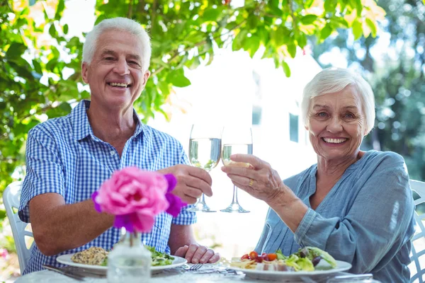 Lächelndes Seniorenpaar prostet Weißwein zu — Stockfoto