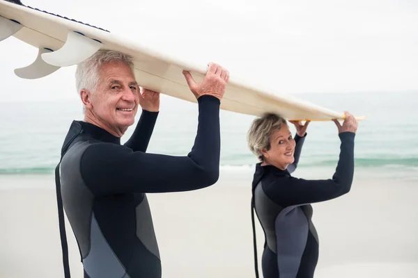 Pareja mayor en traje de neopreno llevando tabla de surf — Foto de Stock