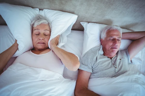Mulher sênior bloqueando as orelhas com travesseiro enquanto o marido ronca — Fotografia de Stock