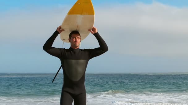 Hombre en traje de neopreno sosteniendo tabla de surf sobre la cabeza — Vídeo de stock