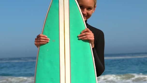 Woman in wet suit hiding behind surfboard — Stock Video