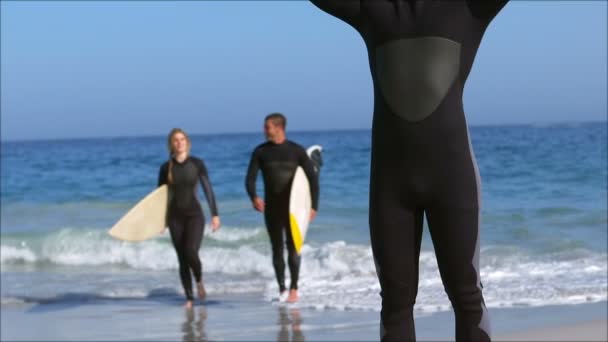 Amigos en traje de neopreno sosteniendo tabla de surf — Vídeo de stock